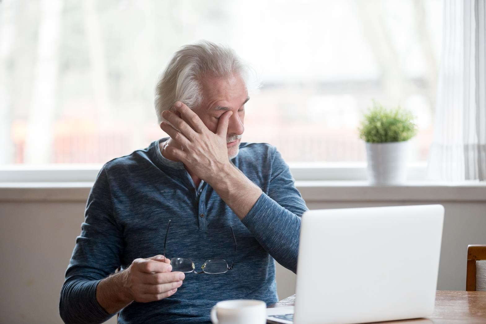 Senior Man Experiencing Dry Eye Symptoms Elderly man with dry eye discomfort looking at laptop screen.